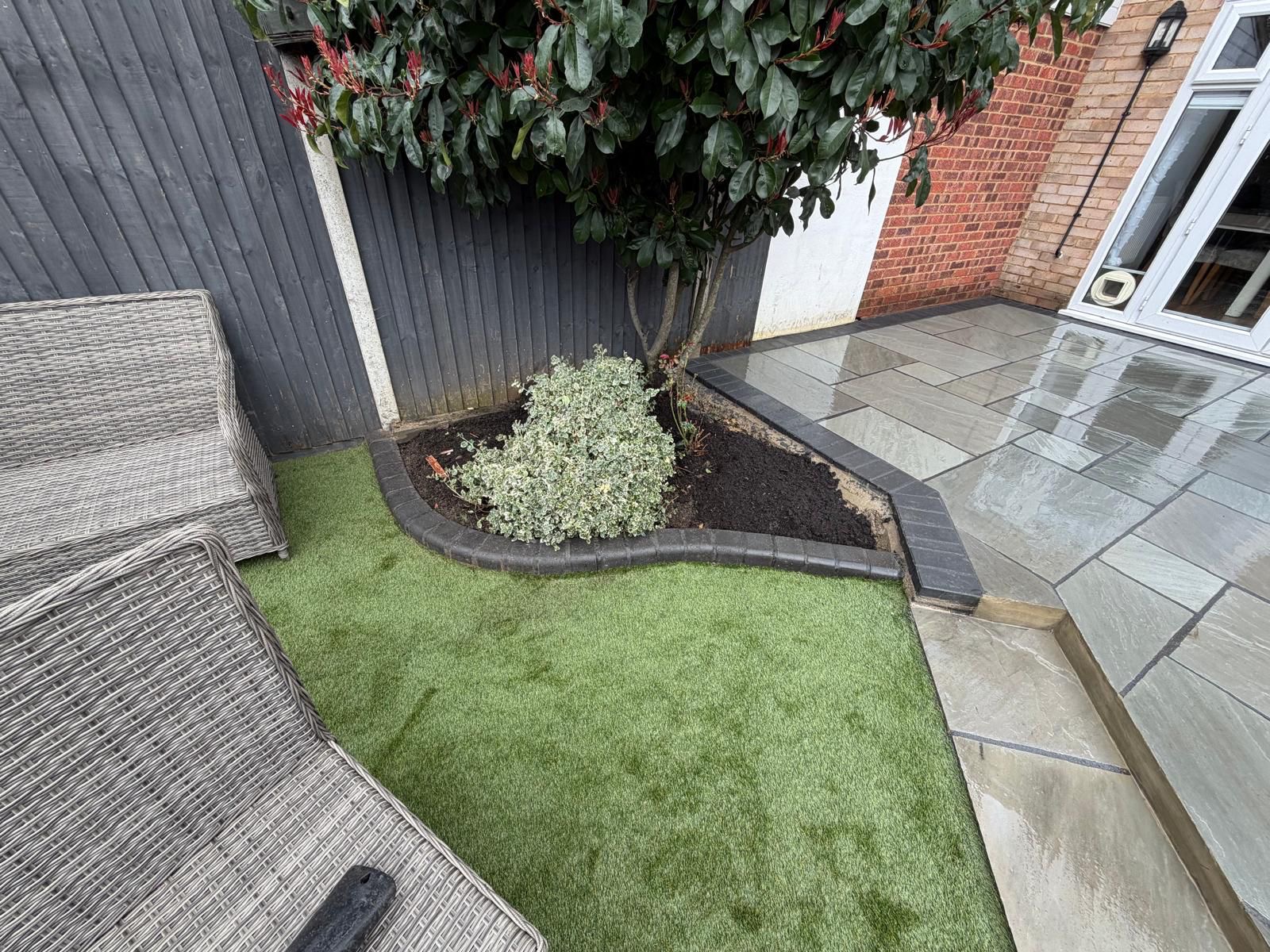 Curved planting bed with charcoal kerb, lawn and patio